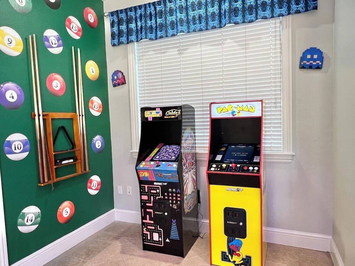 Una stanza con due cabinati arcade, un tavolo da biliardo e una finestra con persiane.