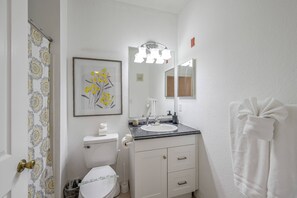 Et badeværelse med toilet, vask, underskab og et håndklædetørrestativ.