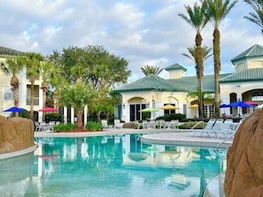 A swimming pool with lounge chairs and umbrellas, surrounded by palm trees and a building with a tiled roof. - Ld12108 - 4BR Apartment Near Disney (Kissimmee)