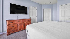 A bedroom with a bed, a dresser, a television mounted on the wall, and two doors. - Th130 - 3BR House Near Disney and Universal Parks (Orlando)