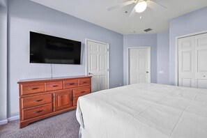Ein Schlafzimmer mit einem Bett, einem Schminktisch, einem an der Wand montierten Fernseher und zwei Türen.