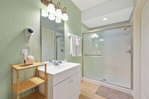 A bathroom with a white vanity, a glass shower enclosure, and a hairdryer mounted on the wall. - Th130 - 3BR House Near Disney and Universal Parks (Orlando)