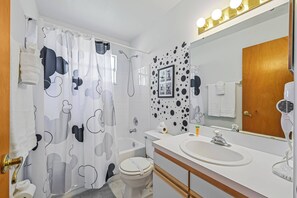 A bathroom with a shower curtain, toilet, sink, and a mirror with lights. - Sw40 - 3BR Apartment Near Disney With Resort Pool (Kissimmee)