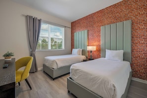 Habitació d'hotel amb dos llits, una taula amb cadira, una làmpada i una paret de maó.