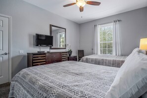Quarto com duas camas, ventoinha no teto, televisão e janela com cortinas.