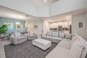 A modern living room with grey sofas, a white coffee table, and a grey rug. There is a dining area with a table and chairs, and a kitchen in the background. - Cg1569 - 5BR House With Pool Near Disney Parks (Davenport)