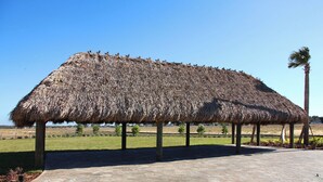 A thatched-roof structure supported by wooden posts, situated on a paved area with a clear sky in the background. - Cg1569 - 5BR House With Pool Near Disney Parks (Davenport)