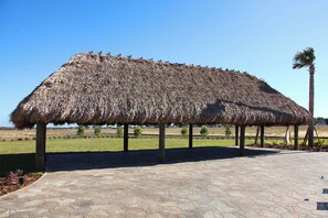 A thatched-roof structure supported by wooden posts, situated on a paved area with a clear sky in the background. - Cg1569 - 5BR House With Pool Near Disney Parks (Davenport)