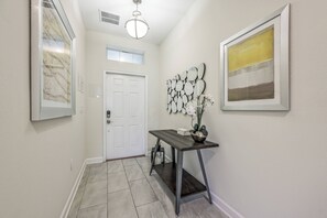 A hallway with a white door, a wall-mounted mirror display, and a framed abstract painting. - Cg1569 - 5BR House With Pool Near Disney Parks (Davenport)