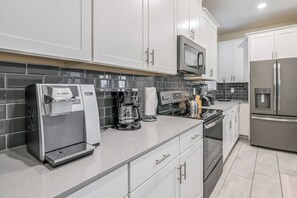 Una cocina moderna con armarios blancos, un refrigerador de acero inoxidable, una cafetera y un microondas.
