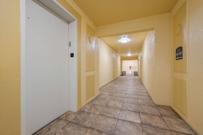 A long, narrow hallway with yellow walls and a tiled floor, leading to a door at the end. - Vc14-407 - 2BR Epic Condo Near Disney (Orlando)