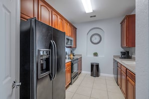 A modern kitchen with wooden cabinets, a stainless steel refrigerator, a microwave, and a sink. - Vc14-407 - 2BR Epic Condo Near Disney (Orlando)