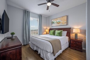 Une chambre d’hôtel avec un lit, des lampes de chevet, un ventilateur de plafond, une télévision et une fenêtre avec des rideaux.