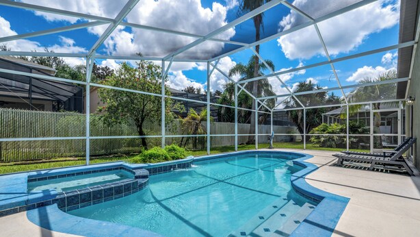 Une piscine entourée d’une clôture et de palmiers, et dotée d’une paroi en verre.