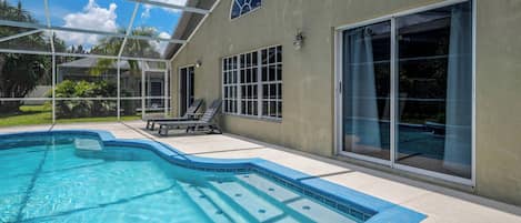 Una piscina con cerramiento de vidrio, un patio con sillones de descanso y un amplio ventanal corredera.
