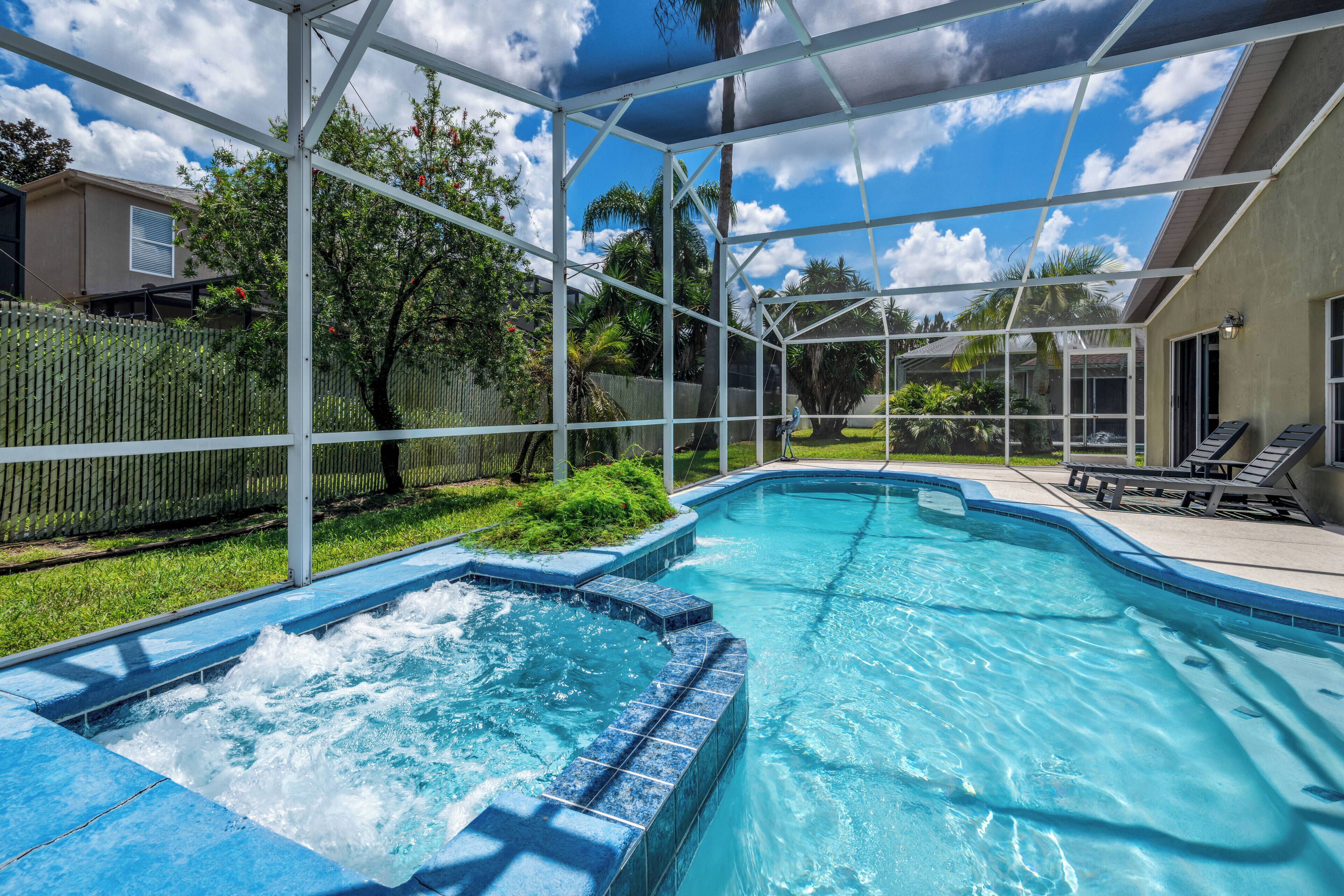 A swimming pool with a hot tub, surrounded by a covered area with a view of a house and trees.