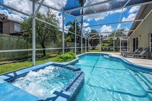 Una piscina con idromassaggio, circondata da una zona coperta con vista su una casa e alberi.
