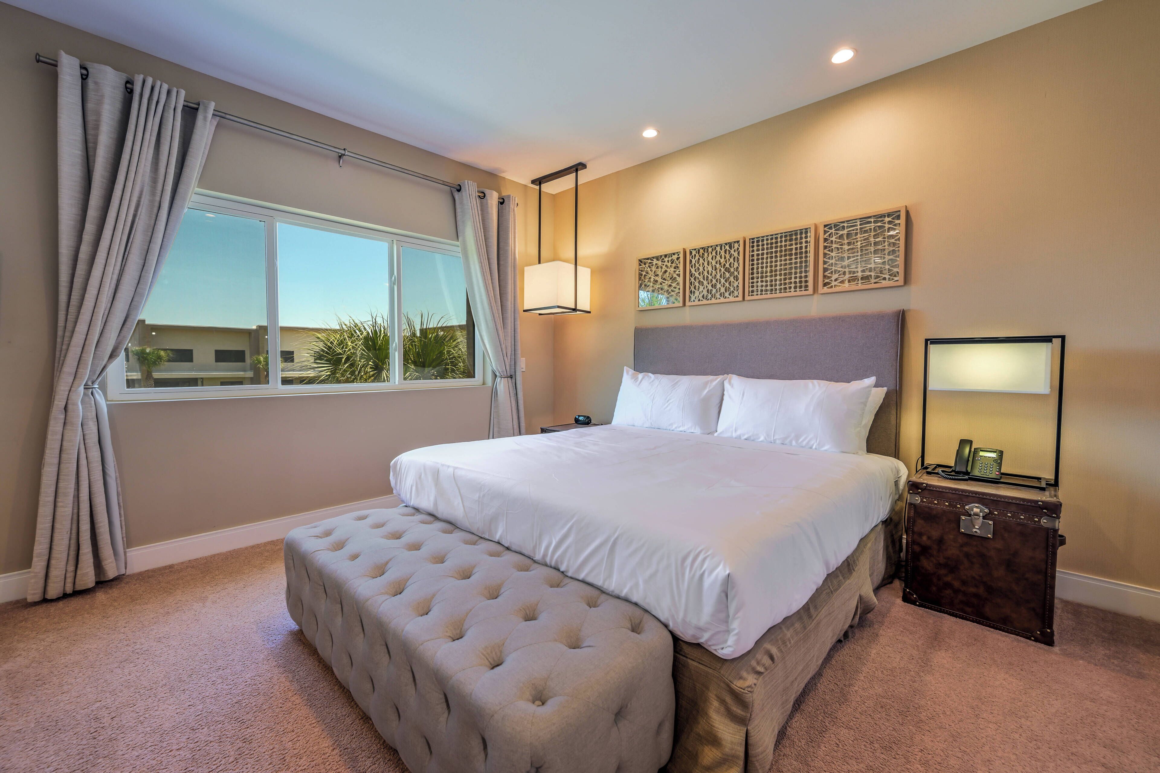 Un dormitorio con una cama grande, una mesita de noche con lámpara, una ventana con cortinas y vistas al exterior.