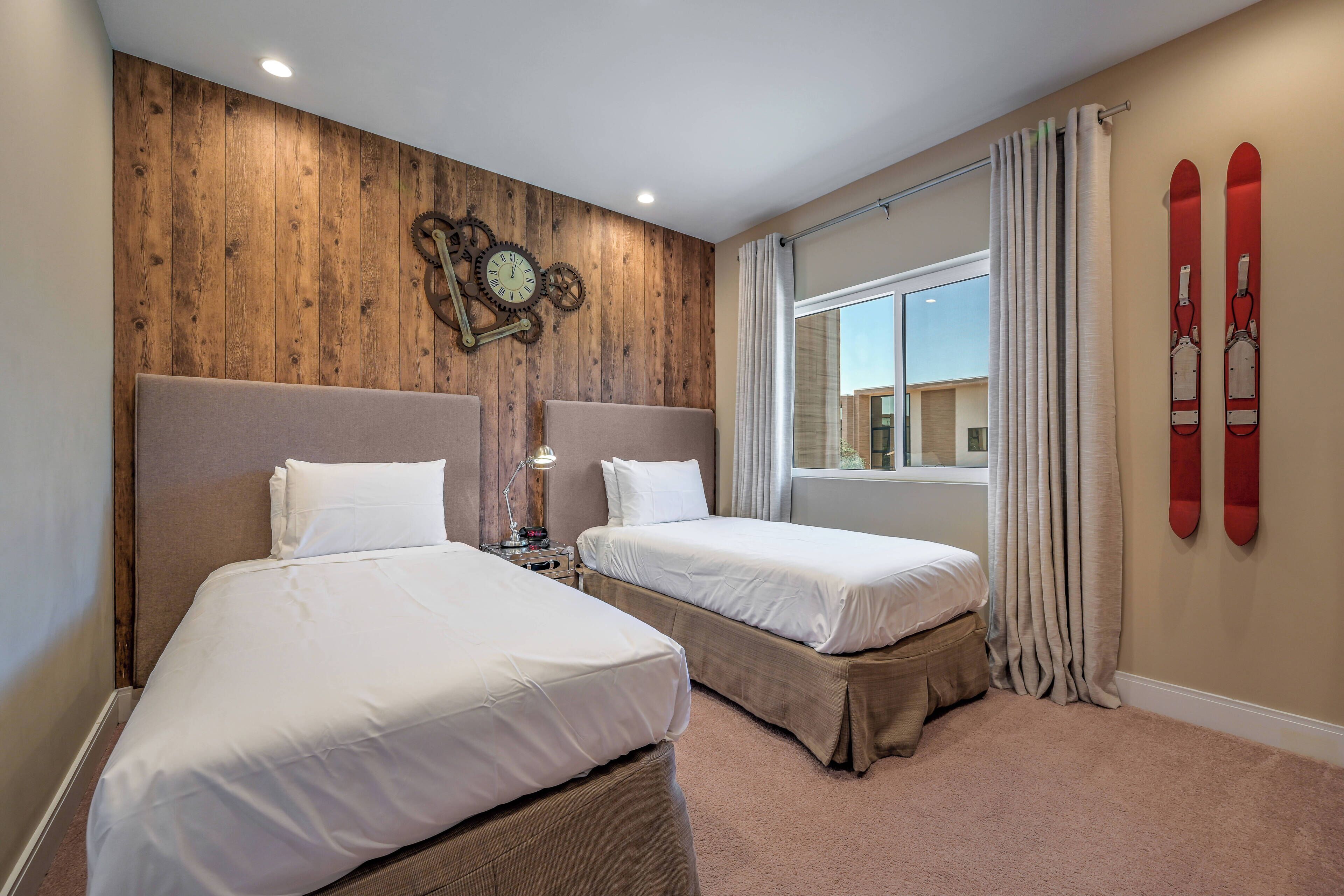 Habitación de hotel con dos camas, paredes de paneles de madera, un reloj, equipo de esquí y una ventana con cortinas.