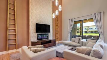 Una sala de estar moderna con una televisión de pantalla plana, sofás color beige, una mesa de centro de madera y una pared decorativa de ladrillo.