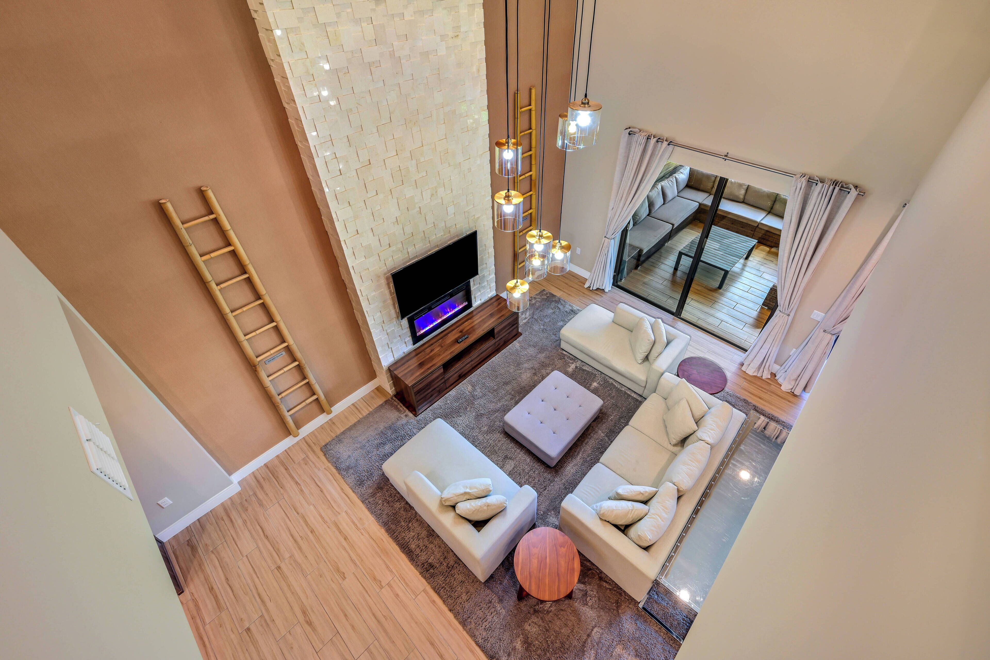 Un salón amplio con televisor de pantalla plana, varios asientos y una escalera decorativa en la pared.