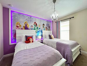 Quarto com duas camas, um candelabro e uma parede decorada com personagens da Disney.