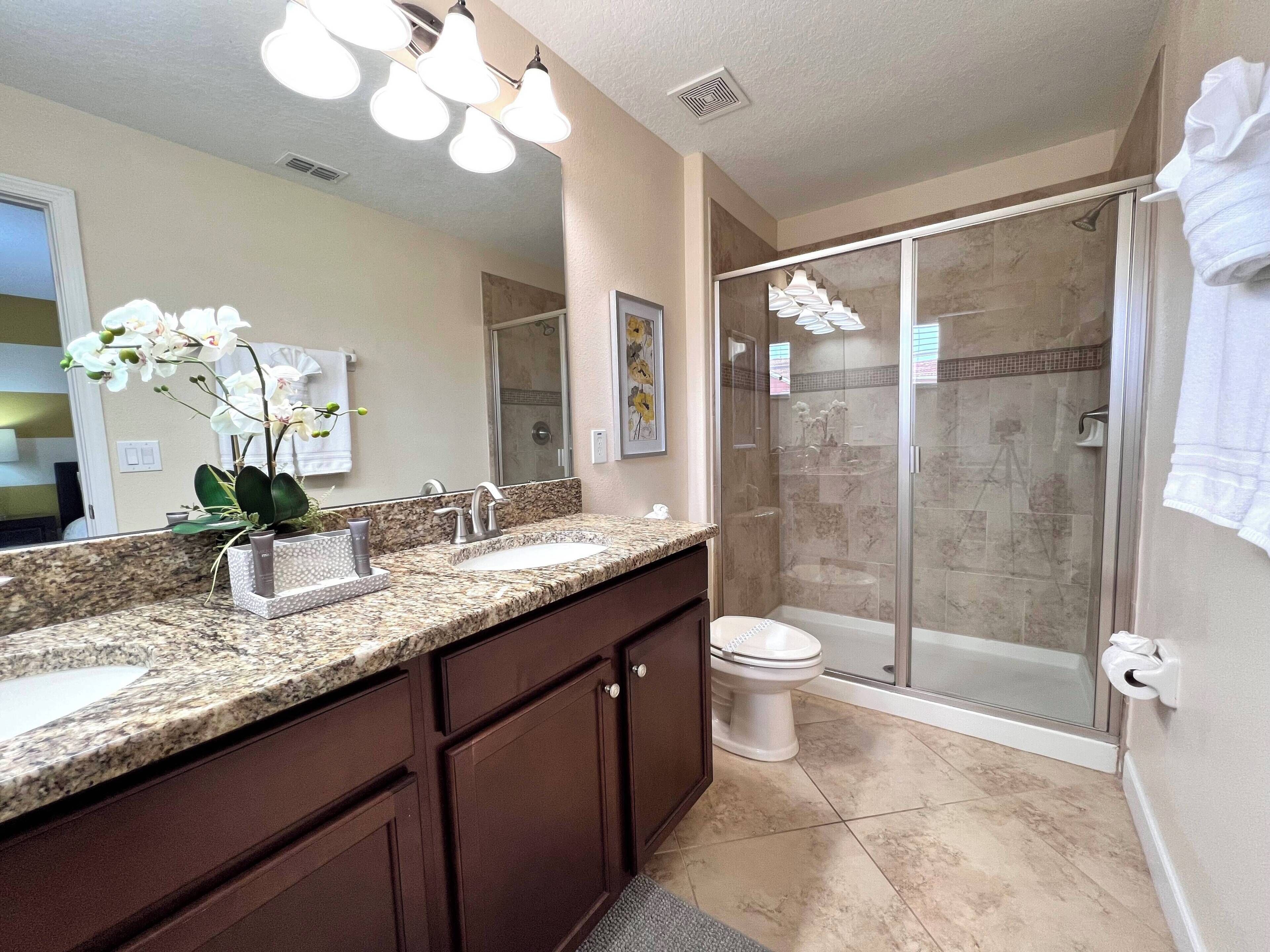 A bathroom with a granite countertop, a sink, a toilet, and a glass-enclosed shower.