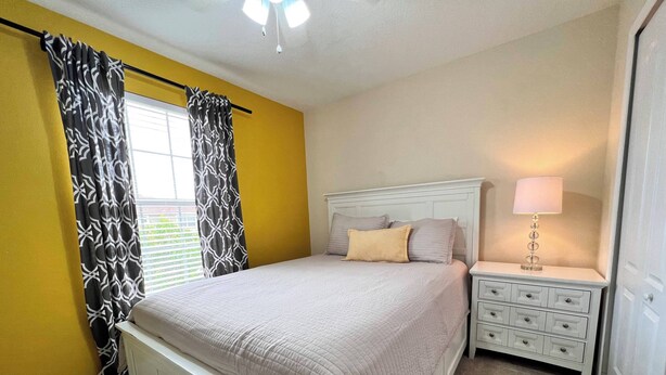 A bedroom with a bed, a nightstand, a lamp, and a window with curtains. - Pp2904 - 6BR House With Pool Near Disney Parks (Kissimmee)