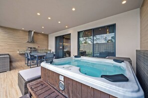A modern outdoor patio with a hot tub, wooden flooring, wicker furniture, and a kitchen area with a chimney. - Mvv7485 - 3BR House Near Disney With Hot Tub (Kissimmee)