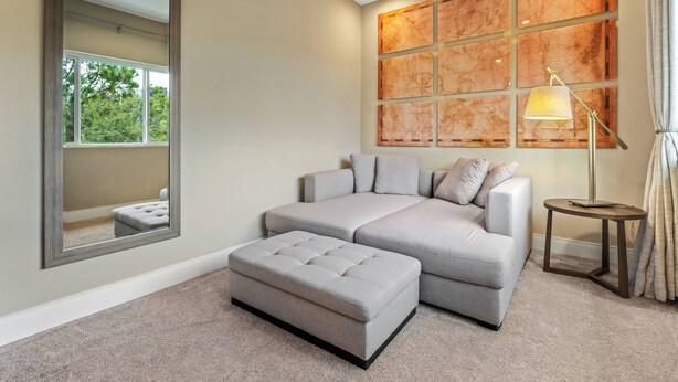 A modern living room with a grey sectional sofa, a matching ottoman, a large mirror, and a floor lamp. - Mvv7485 - 3BR House Near Disney With Hot Tub (Kissimmee)