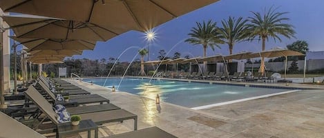 A poolside area with lounge chairs and umbrellas, a pool, and palm trees in the background.