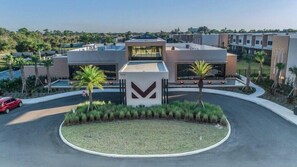 A modern building with a central entrance, surrounded by a landscaped area with palm trees. - Mvv7485 - 3BR House Near Disney With Hot Tub (Kissimmee)