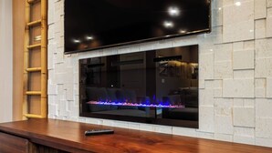A modern living room with a flat-screen TV mounted above a fireplace, a wooden bench, and a ladder against the wall. - Mvv7485 - 3BR House Near Disney With Hot Tub (Kissimmee)