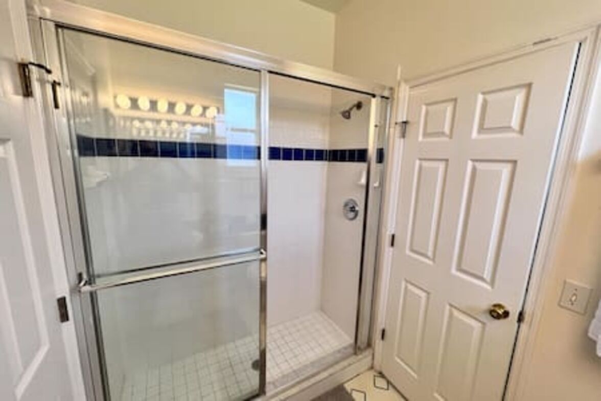 A glass-enclosed shower with a white door and a blue-tiled wall.