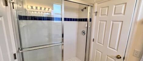 A glass-enclosed shower with a white door and a blue-tiled wall.