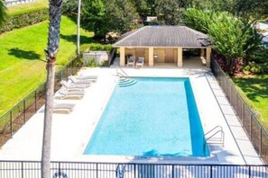 A rectangular swimming pool with a covered area and lounge chairs, surrounded by a fence and greenery. - Sv2925 - 4BR House With Pool Near Disney Parks (Kissimmee)