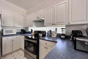 A modern kitchen with white cabinets, a black stove, a microwave, and a coffee maker. - Sv2925 - 4BR House With Pool Near Disney Parks (Kissimmee)