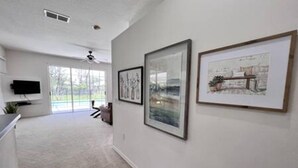 A hallway with framed artwork on the walls, a ceiling fan, and a television mounted on the wall. - Sv2925 - 4BR House With Pool Near Disney Parks (Kissimmee)