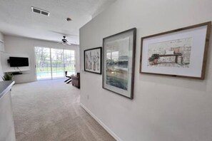 A hallway with framed artwork on the walls, a ceiling fan, and a television mounted on the wall. - Sv2925 - 4BR House With Pool Near Disney Parks (Kissimmee)