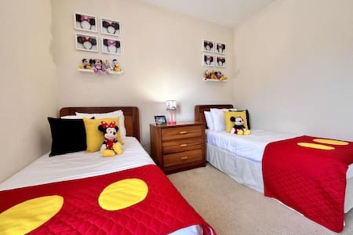 Une chambre avec deux lits, chacun agrémenté de linge de lit aux motifs de Mickey Mouse. On y trouve des étagères murales avec des tableaux et de petites figurines.