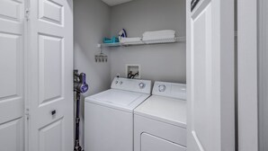Une buanderie équipée de deux machines à laver et deux sèche-linge superposés, d’une étagère où sont pliées les serviettes et d’un panier à linge fixé au mur.