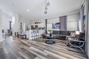 A modern living room with a sofa, coffee table, and dining area. - Hl137 - 5BR House With Pool Near Disney Area (Davenport)