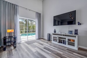 Un salon moderne doté d’un grand téléviseur, d’une console et offrant une vue sur une piscine grâce à de grandes portes vitrées.