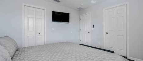 A bedroom with a bed, a ceiling fan, a mounted TV, and white doors.