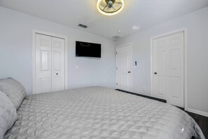 Une chambre à coucher avec un lit, un ventilateur de plafond, un téléviseur fixé au mur et des portes blanches.