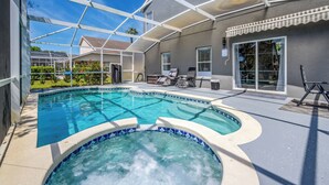Une piscine avec un jacuzzi, entourée d’un patio couvert aménagé avec du mobilier d’extérieur.