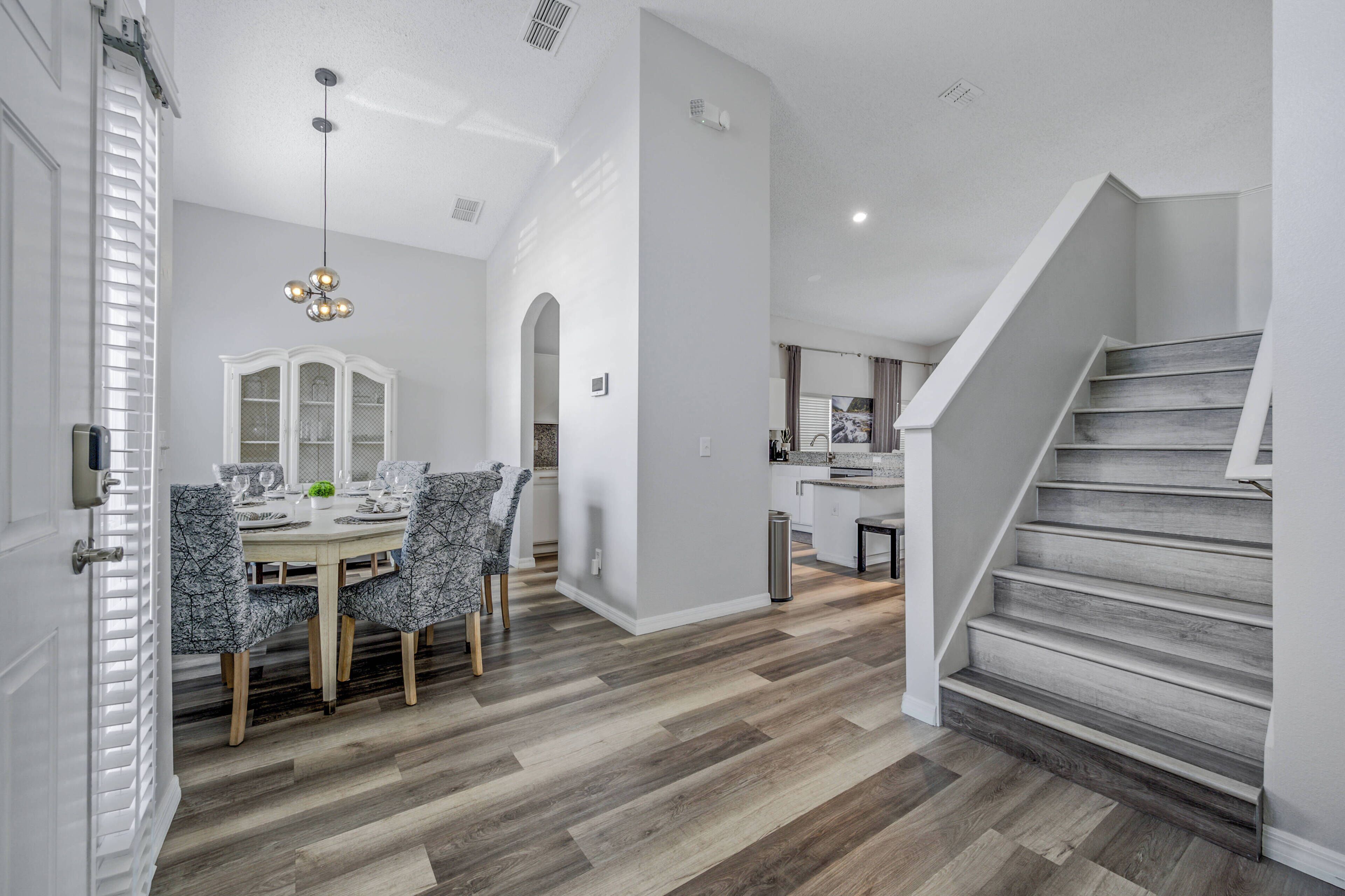 A modern kitchen with white cabinets, a dining area with a round table and patterned chairs, and a staircase with wooden steps.