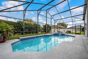 Ein Schwimmbecken mit blauer Fliesenverkleidung, umgeben von einem Metallzaun, mit einer Rasenfläche, Bäumen und einem Haus im Hintergrund.