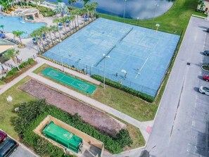 Ein großer Außen-Tennisplatz mit Pool und einem kleineren, angrenzenden Platz, umgeben von Grünflächen und einem Parkplatz.