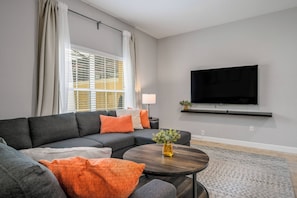 A modern living room with a sectional sofa, a round coffee table, and a flat-screen TV mounted on the wall. - Pp8962 - 4BR House With Pool Near Disney Parks (Kissimmee)